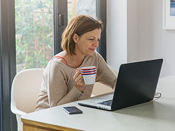 Woman holding a mug whilst at her laptop