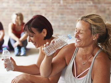 Two women smiling and drinking water during an exercise class