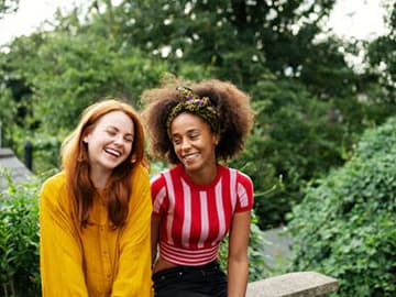 Two teenage girls sat on a wall and smiling