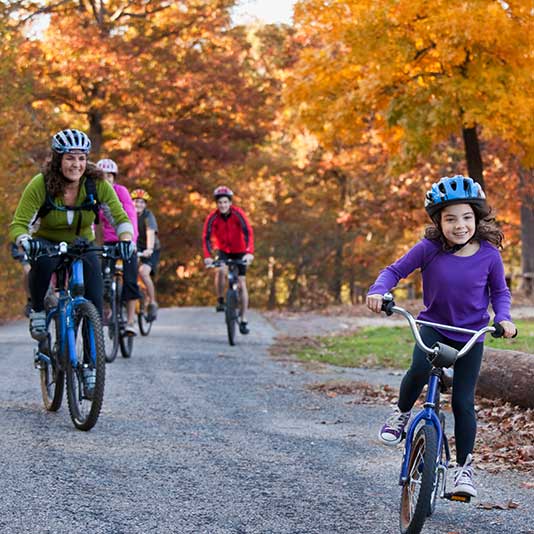 A family riding bikes through an autumnal forest path