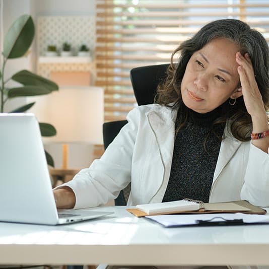 Woman looking fed-up whilst working at laptop