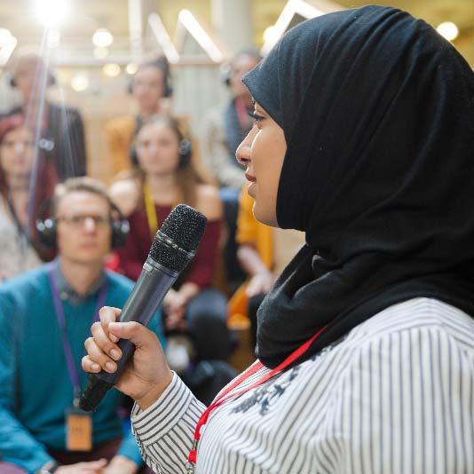 Woman wearing a hijab and speaking to a crowd using a microphone