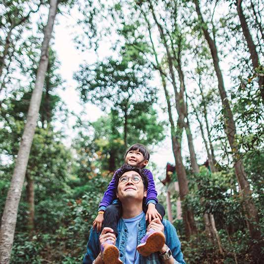 Father carrying daughter on his shoulders, walking through forest