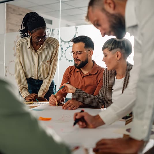 Four people collaborating around a table, discussing and writing on papers