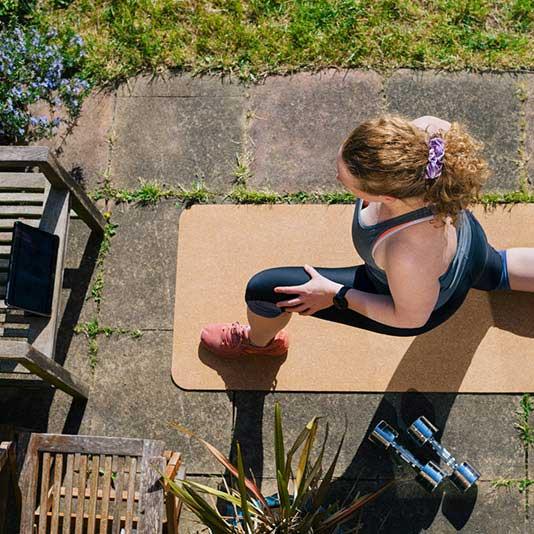 A woman stretching on a yoga mat on her garden patio