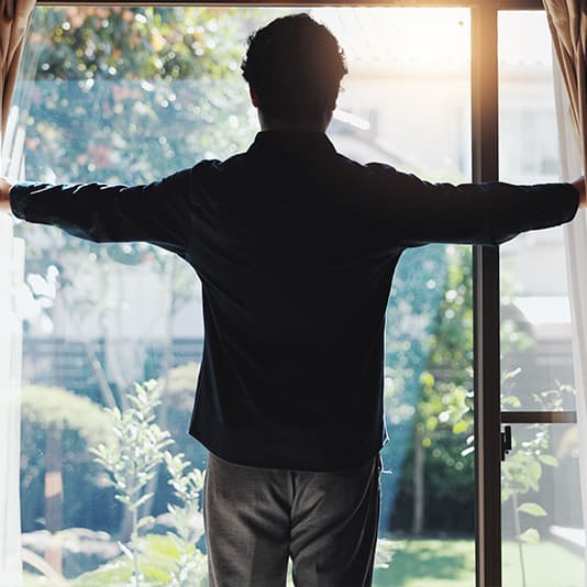 Man opening curtains with sunlight shining