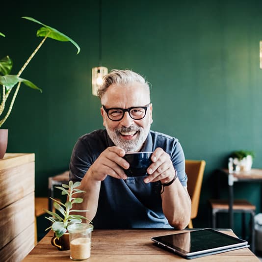 Smiling man with glasses holding a mug, sitting at a table