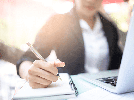 Woman writing on notepad at laptop