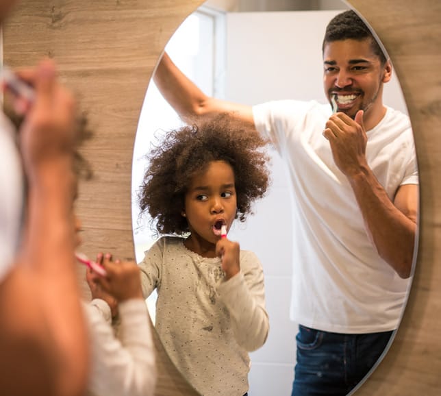 Father and child brushing their teeth together in the mirror