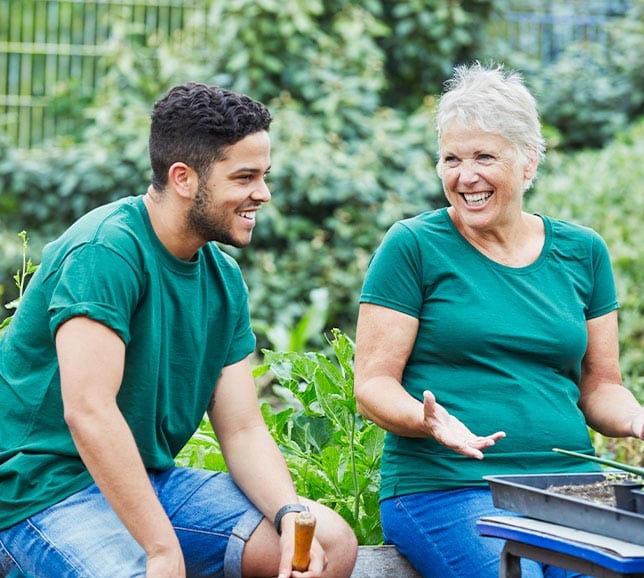 Two people sat in a garden, smiling and potting plants
